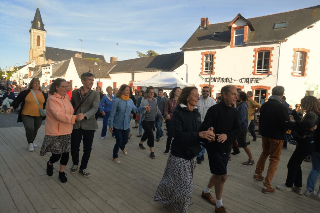 Gens dansant sur place dans village, église en fond